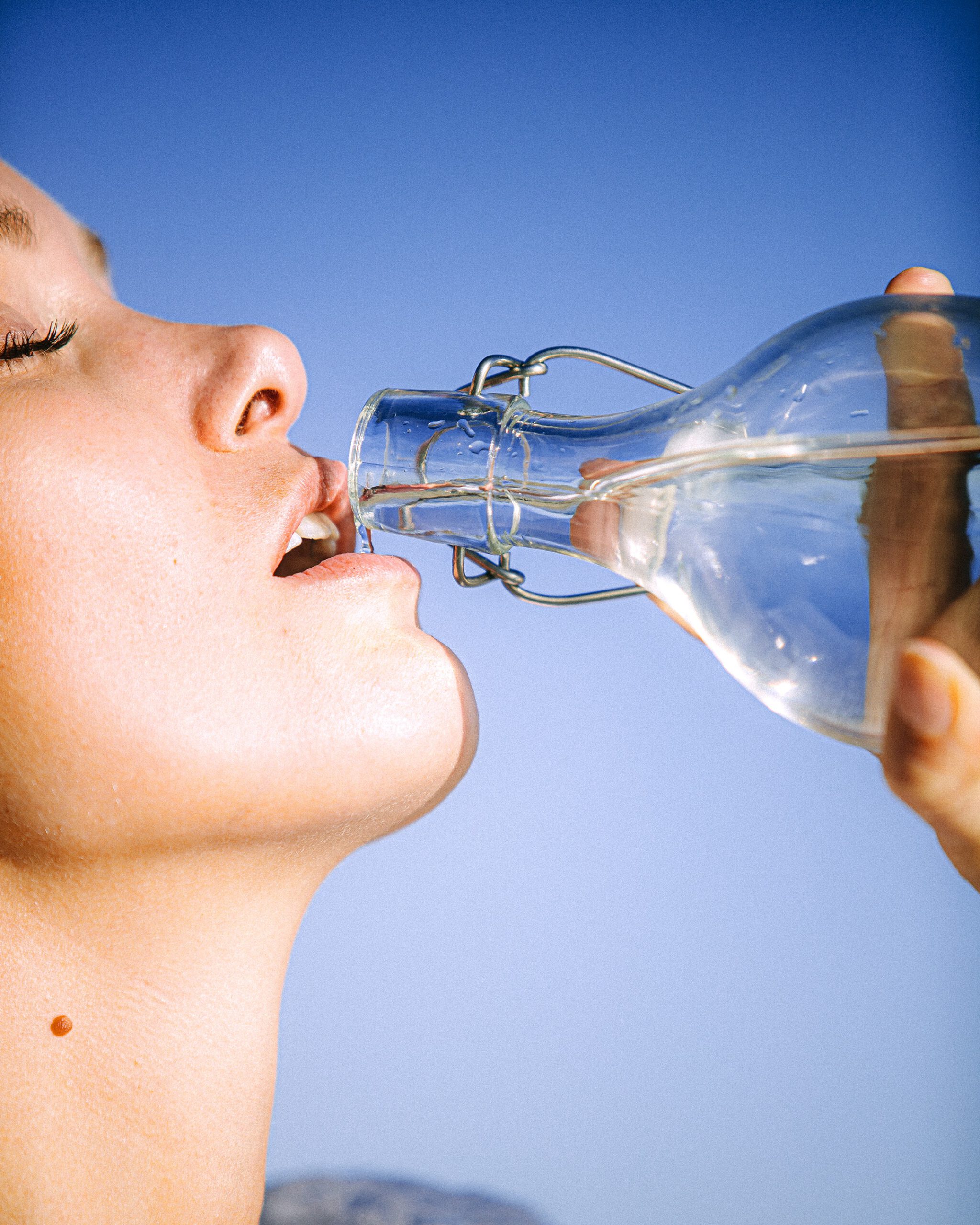 Vrouw drink water uit glazen fles.